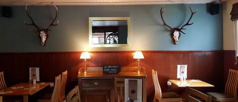 A restaurant interior with wooden paneling, two tables with chairs, and antler skulls mounted on the wall.