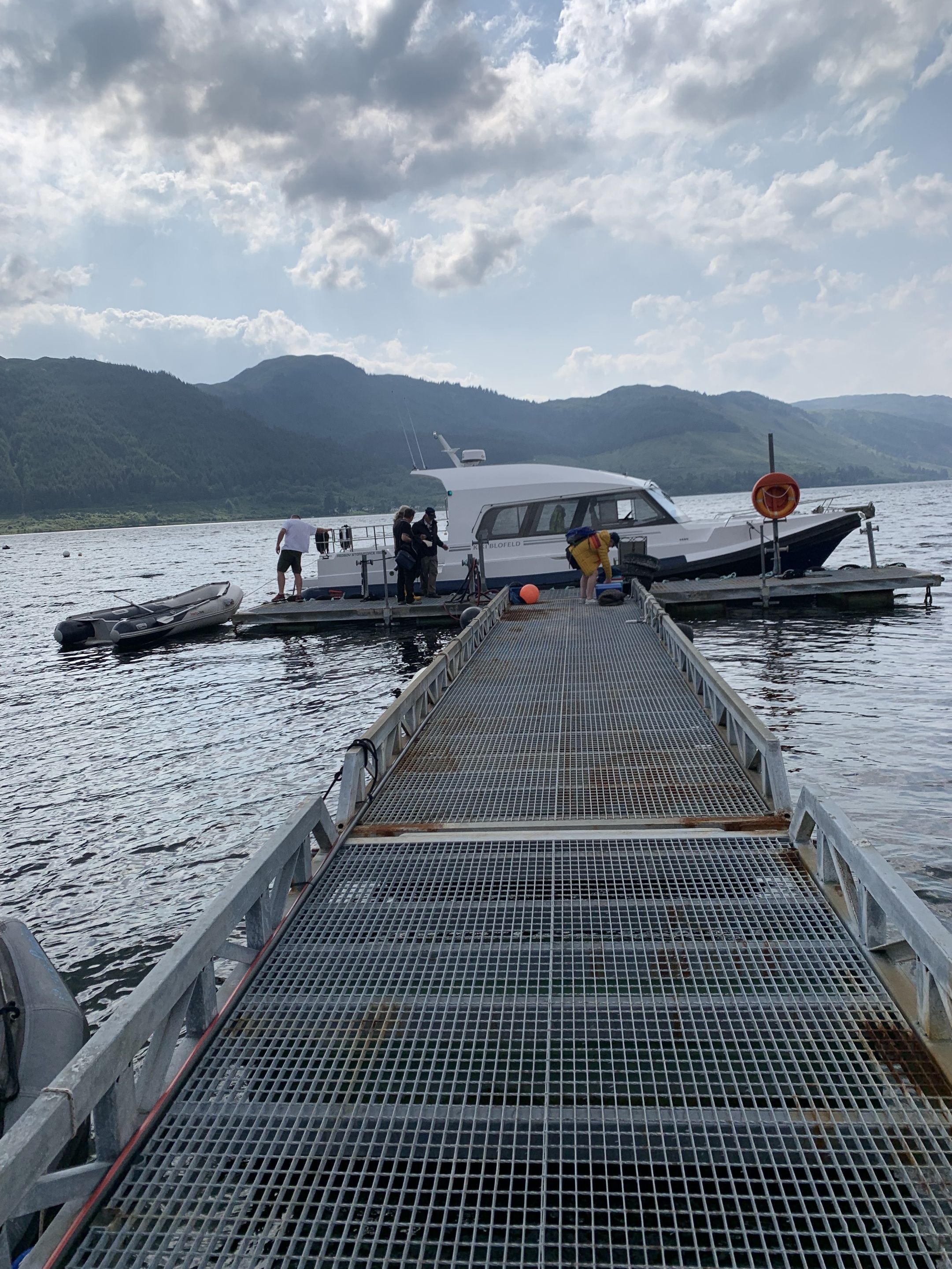 A dock with a boat, a person standing, and a mountainous landscape in the background.