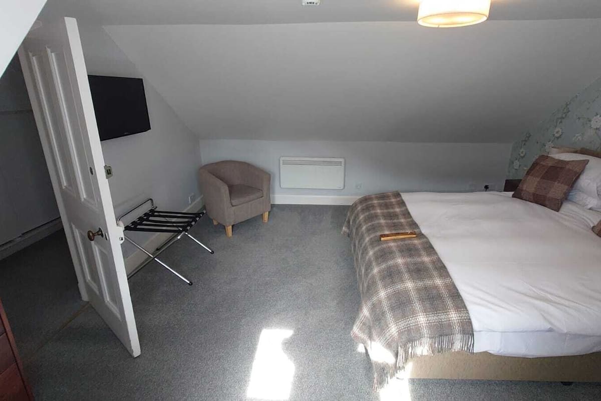 A bedroom with a bed, a chair, a radiator, and a wall-mounted TV.