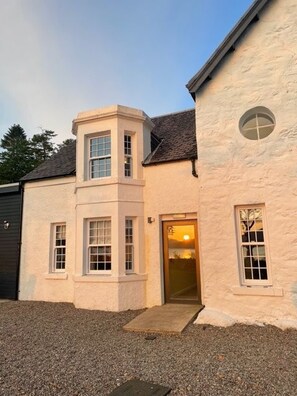 A building with a beige facade, a small entrance, and a window with a view. - Kintail Lodge Hotel (Kyle)