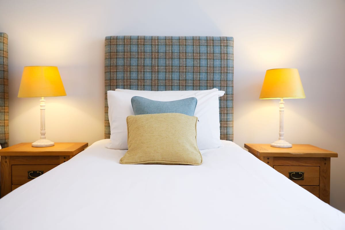 A neatly made bed with white linens, two bedside lamps, and a plaid headboard.