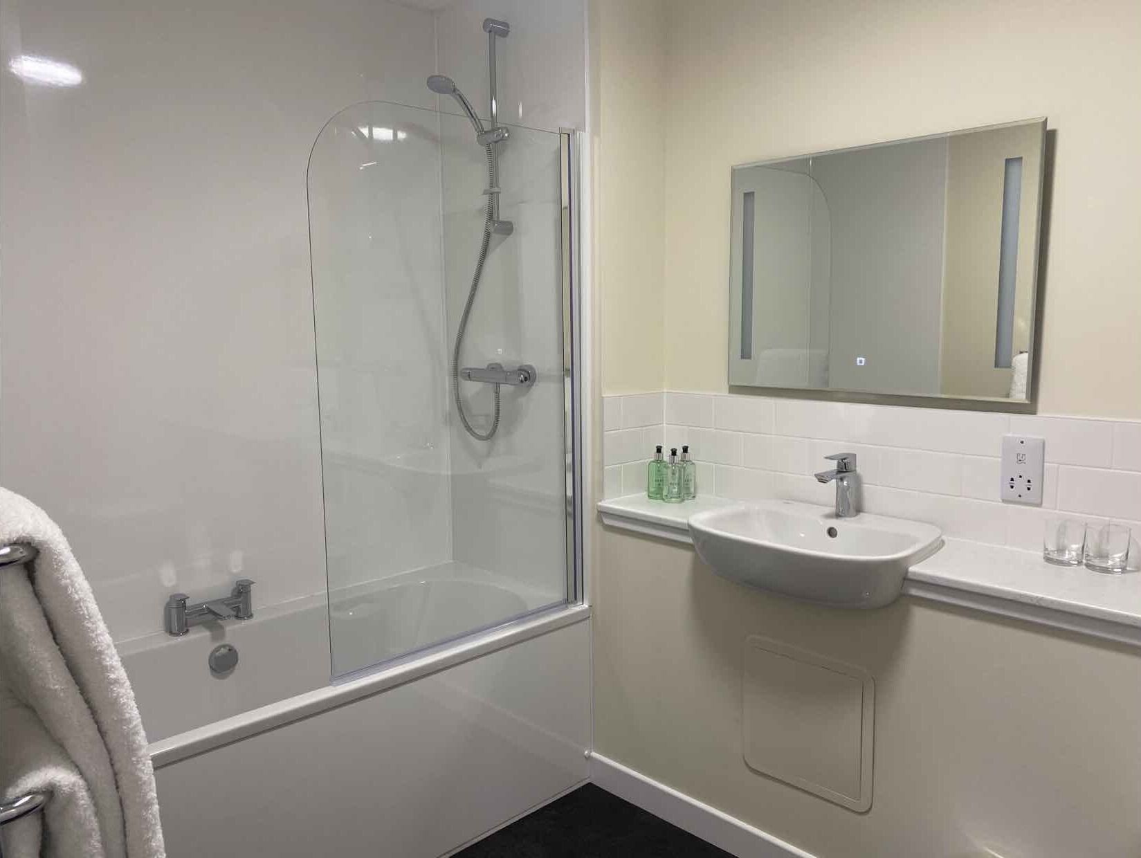Een moderne badkamer met een douchecabine van glas, een witte wastafel en een spiegel erboven.