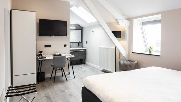 A modern apartment with a kitchenette, a dining area, a large bed, and a TV mounted on the wall. - Hotel L'ARTiste (Lessines)