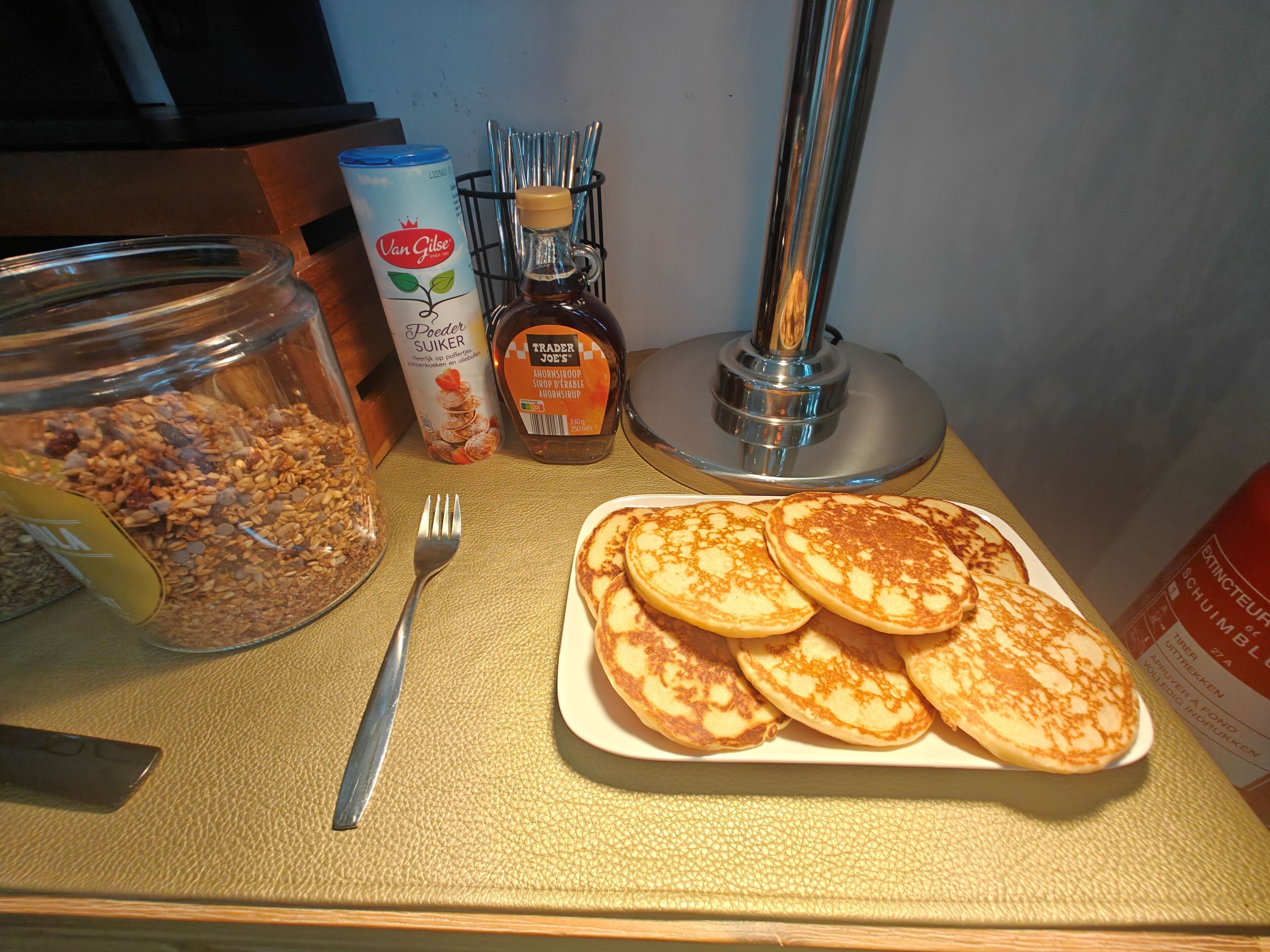 Ett frukostbord med müsli, en burk honung, en honungssked och en tallrik med pannkakor.