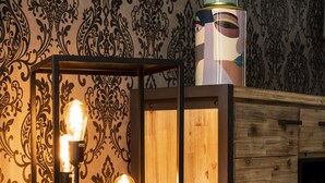 A modern room with a wooden cabinet, a decorative wall, and three illuminated light fixtures on a black metal stand. - Hotel L'ARTiste (Lessines)
