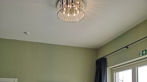 A modern living room with a green sofa, a flat-screen TV, a ceiling light fixture, and a window with a view of the outside. - Hotel L'ARTiste (Lessines)