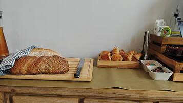 En skærebræt med et brød og en kniv, en træbakke med croissanter, og en lille skål med nødder.