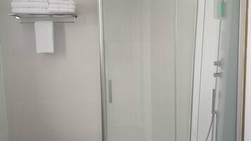 Een moderne badkamer met een douchecabine van glas, een betegelde muur in het wit, een klein plankje met opgevouwen handdoeken en een witte prullenbak.