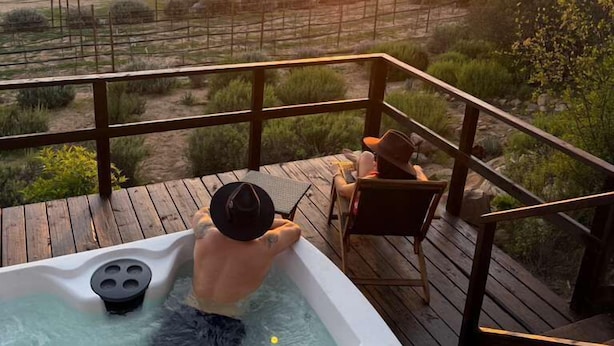 Ein Whirlpool auf einer Holzterrasse mit Blick auf einen Sonnenuntergang über einer ländlichen Landschaft.