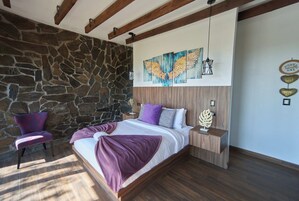 Un dormitorio con pared de piedra, una cama con manta púrpura, una mesita de noche y una silla.