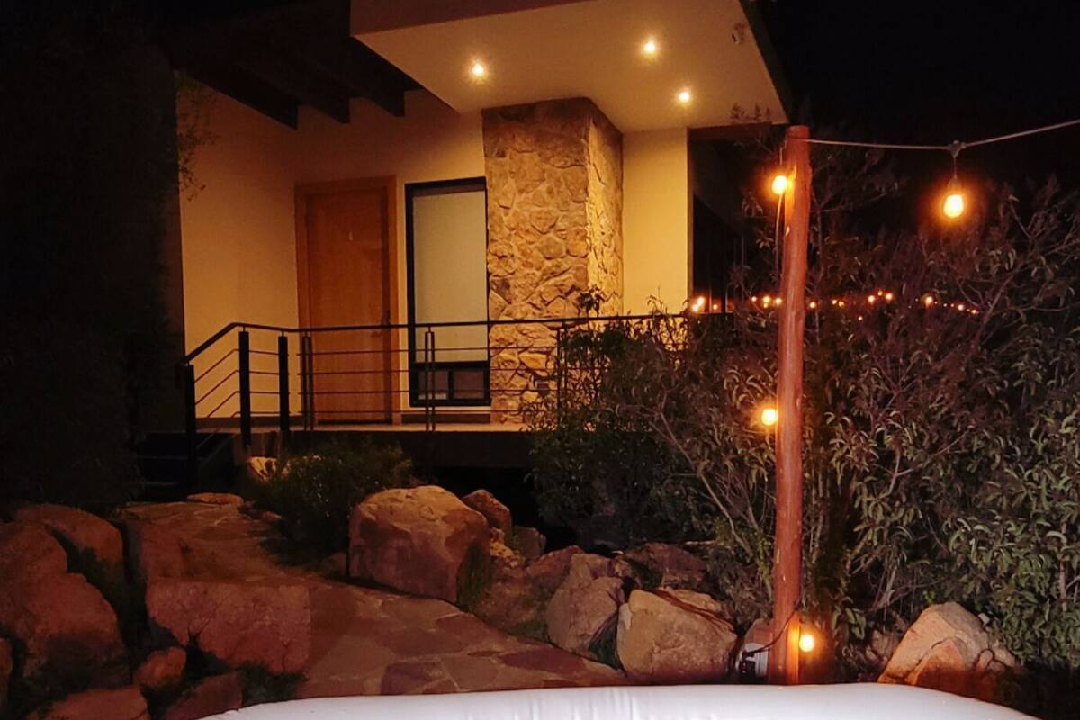 A hot tub in front of a stone building with a wooden deck and a staircase leading to a door.