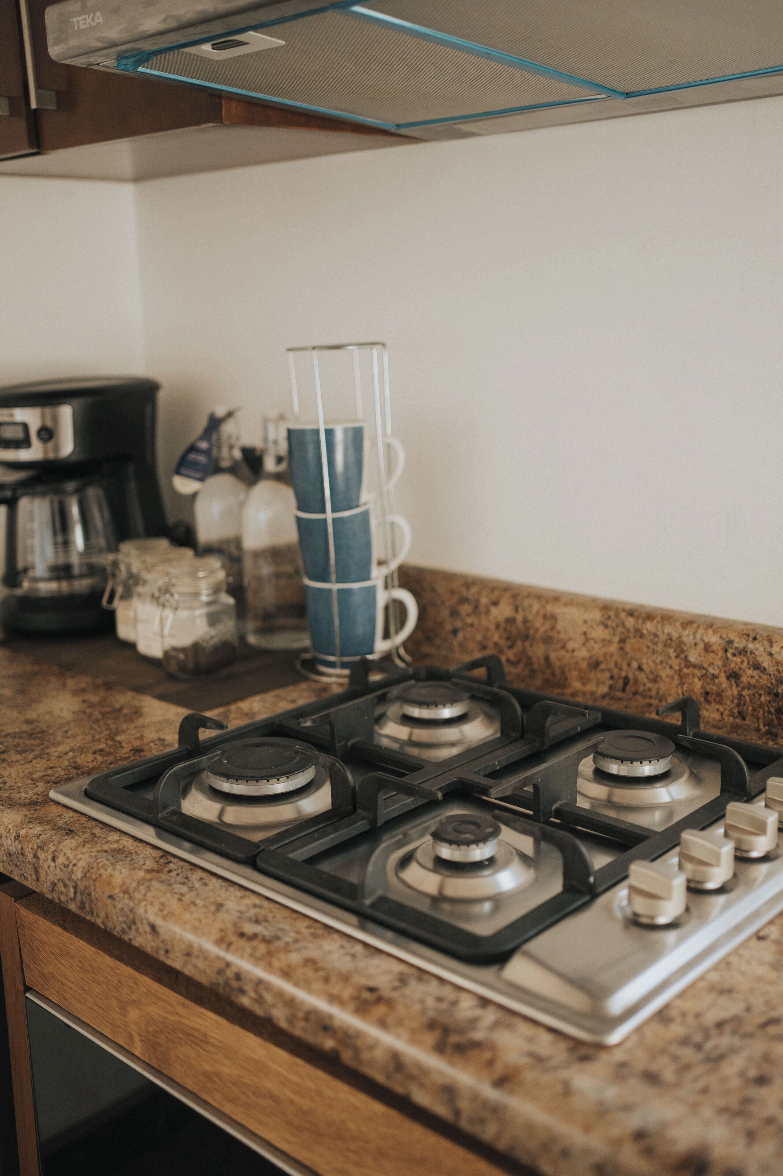 A kitchen with a gas stove, a coffee maker, and stacked blue cups.