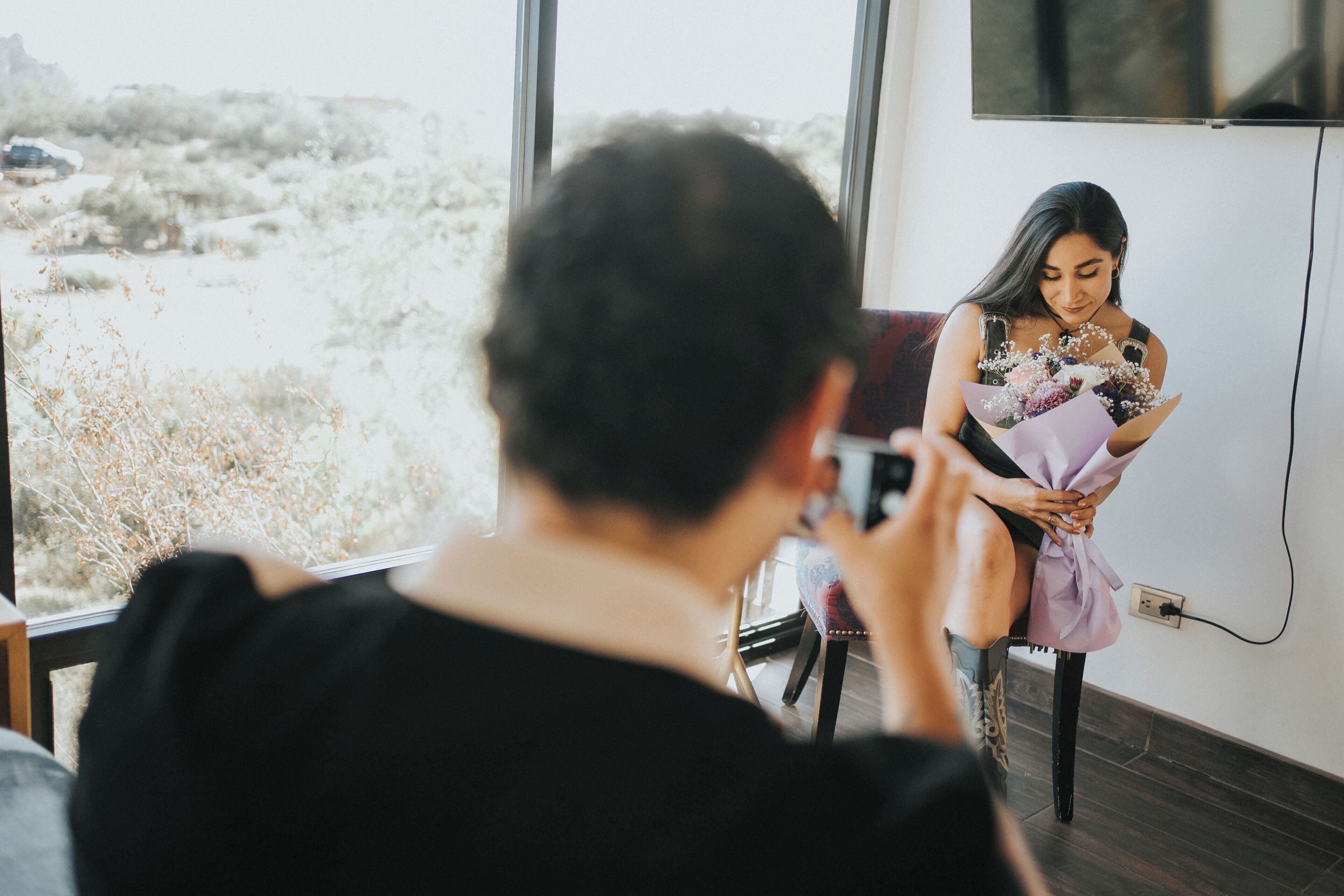 Eine Person fotografiert eine andere Person, die an einem Fenster mit Blick auf eine Wüstenlandschaft sitzt.