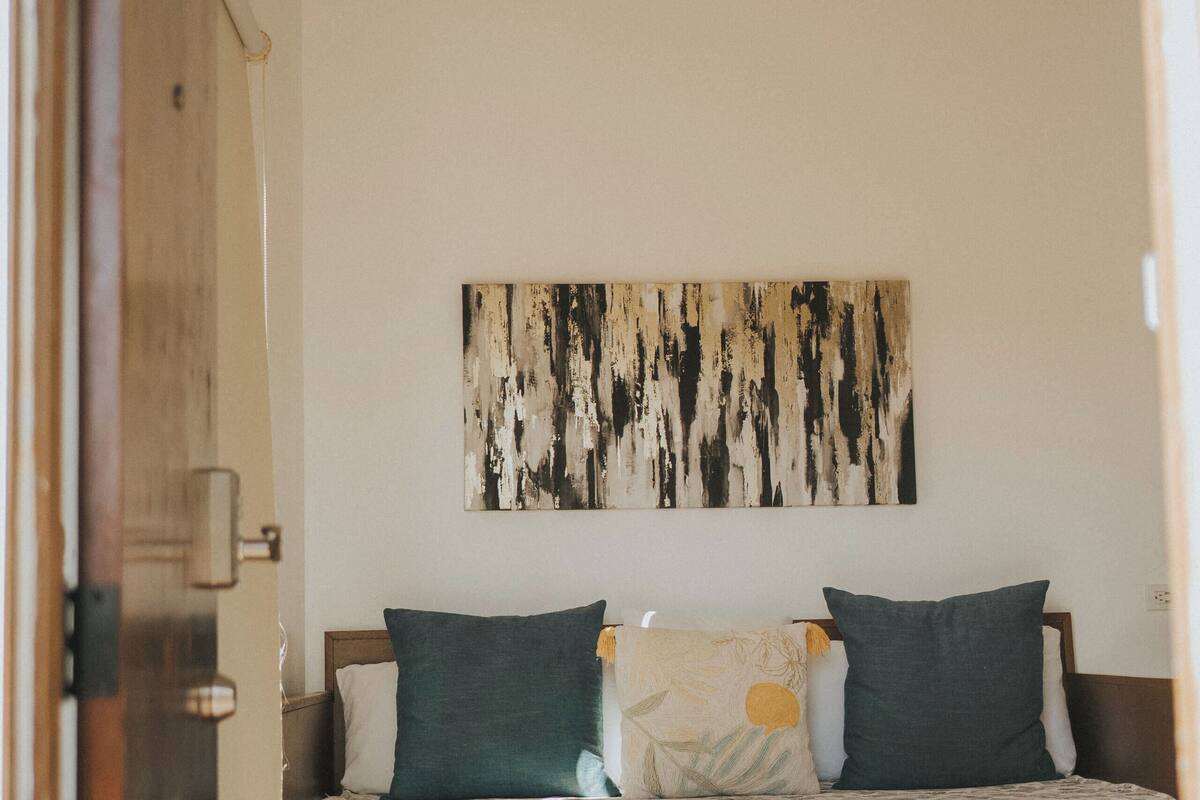 A bedroom with a wooden bed, two pillows, a wall-mounted abstract painting, and a wooden door.