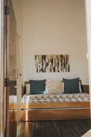 Un dormitorio con cama de madera, dos almohadas, un cuadro abstracto colgado en la pared y una puerta de madera.
