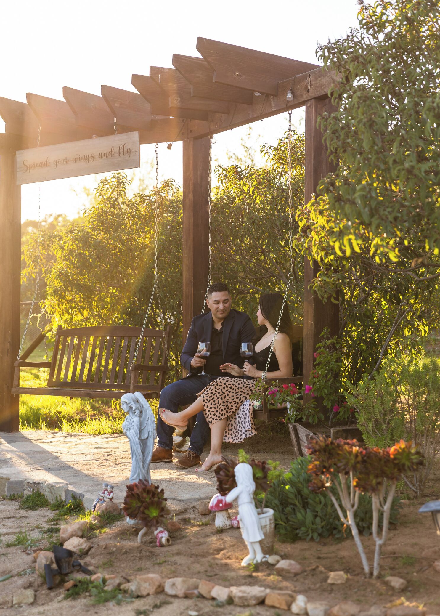 A wooden swing set with a bench, surrounded by greenery and garden decorations.