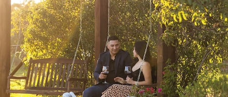 A wooden swing set with a bench, surrounded by greenery and garden decorations.