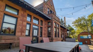 Un edificio in mattoni con un'ampia terrazza in legno, posti a sedere all'aperto e luci decorative.