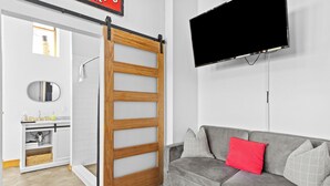 Un bagno moderno con una porta scorrevole in legno, un divano grigio con cuscini rossi e bianchi e una TV a parete.