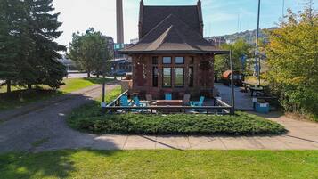 A small brick building with a sloped roof, surrounded by a wooden deck with outdoor seating.