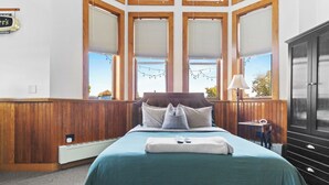 Una camera d'albergo con un letto grande, pannelli in legno, diverse finestre e vista sull'esterno.