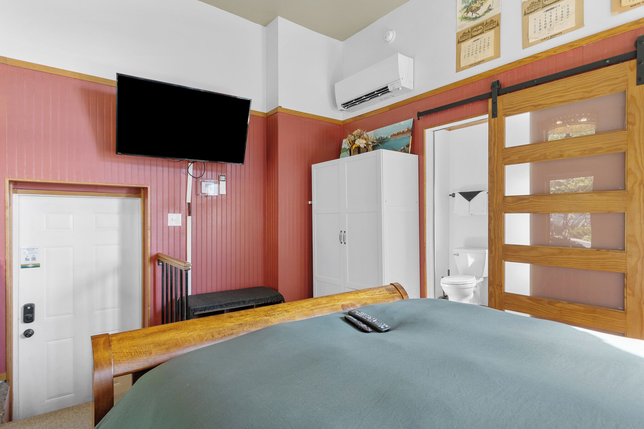 A bedroom with a bed, a television mounted on the wall, a wardrobe, a sliding door, and a window.