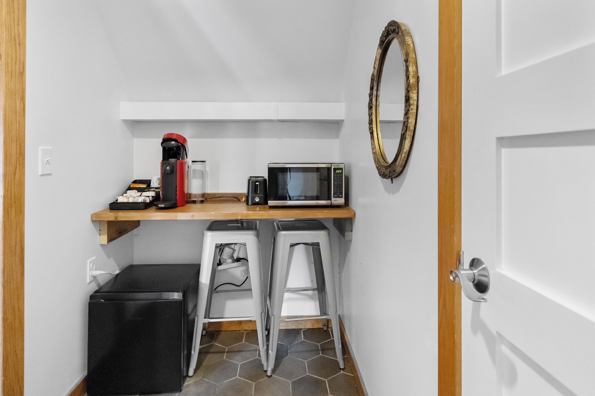 A compact kitchenette with a microwave, coffee maker, and two stools.