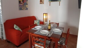 Un área de comedor con un sofá rojo, mesa de madera dispuesta con platos, vasos y una botella.