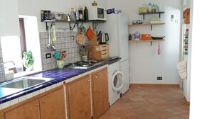 Cocina con armarios de madera, un lavamanos, un microondas y una lavadora. Hay repisas con diversos utensilios de cocina y un reloj en la pared.