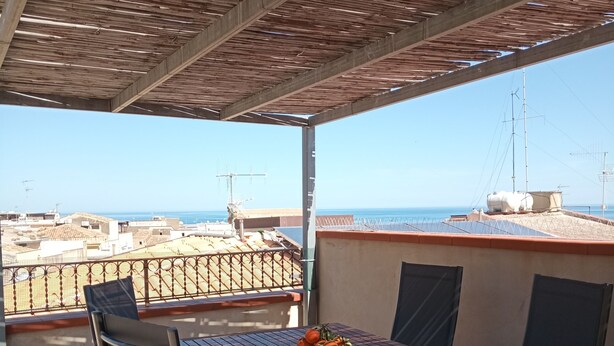 Un espacio de estar al aire libre cubierto con una mesa y sillas, con vistas a la ciudad y al mar.