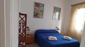 Un dormitorio con colcha azul, ventilador de techo y dos carteles en la pared.