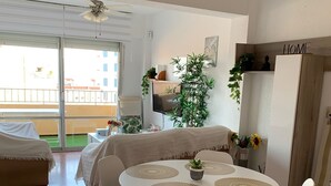 Ein modernes Wohnzimmer mit einem runden Esstisch, weißen Stühlen, einem Deckenventilator, einem großen Fenster und einem Balkon.