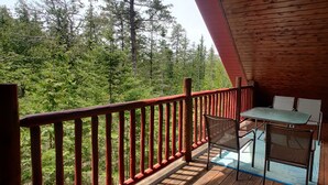 A wooden balcony with a table and chairs, overlooking a forested area. - Tobermory Peaceful Private Entire Log Cottage Spacious Fully Equipped (Tobermory)