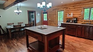 A wooden cabin interior with a dining area, kitchen, and a large window overlooking greenery. - Tobermory Peaceful Private Entire Log Cottage Spacious Fully Equipped (Tobermory)