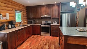 A modern kitchen with wooden cabinetry, stainless steel appliances, and a large window. - Tobermory Peaceful Private Entire Log Cottage Spacious Fully Equipped (Tobermory)
