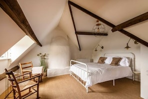 Un dormitorio con techo inclinado, una cama, una silla y una mesita.