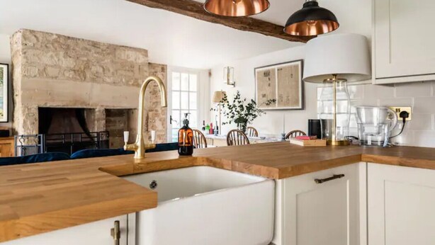 Eine moderne Küche mit Kamin aus Stein, Holz Arbeitsplatten und Pendelleuchten aus Kupfer.