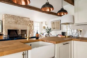 Una cocina moderna con chimenea de piedra, encimeras de madera y lámparas colgantes de cobre.
