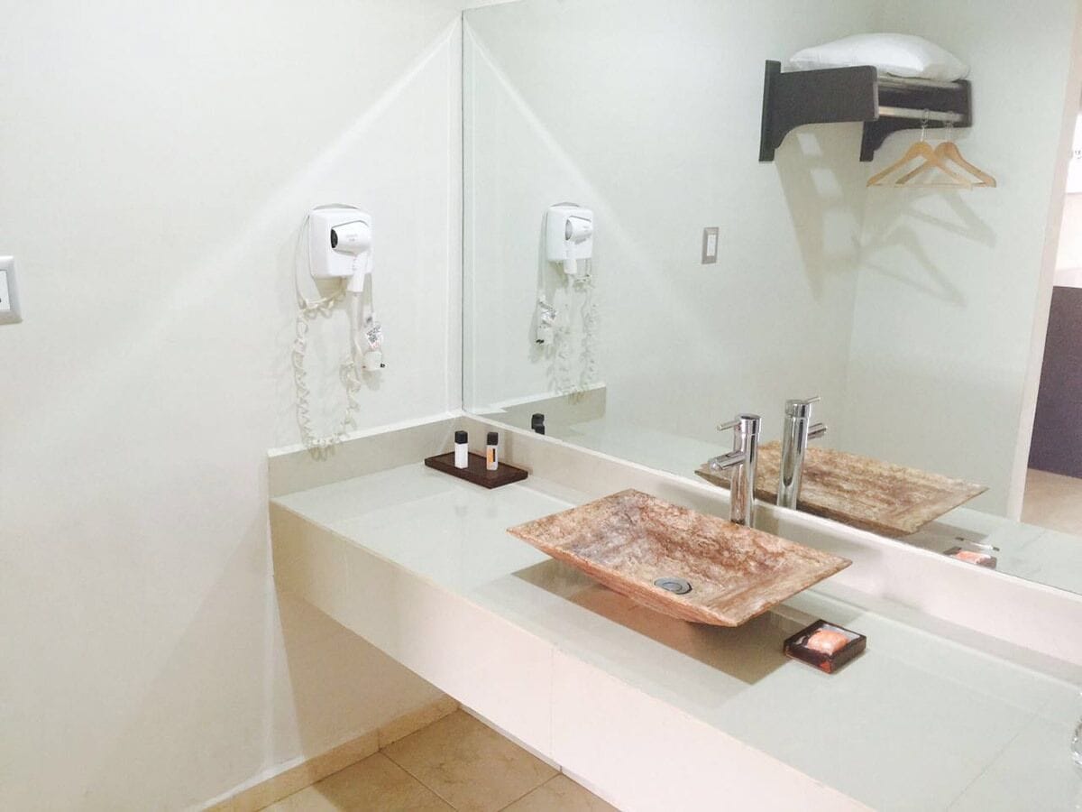 A bathroom with a large mirror, two sinks with square, textured basins, a towel rack, and a wall-mounted hairdryer.