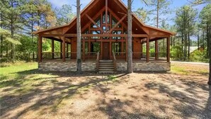 A wooden cabin with a triangular roof, a stone foundation, and a covered porch.