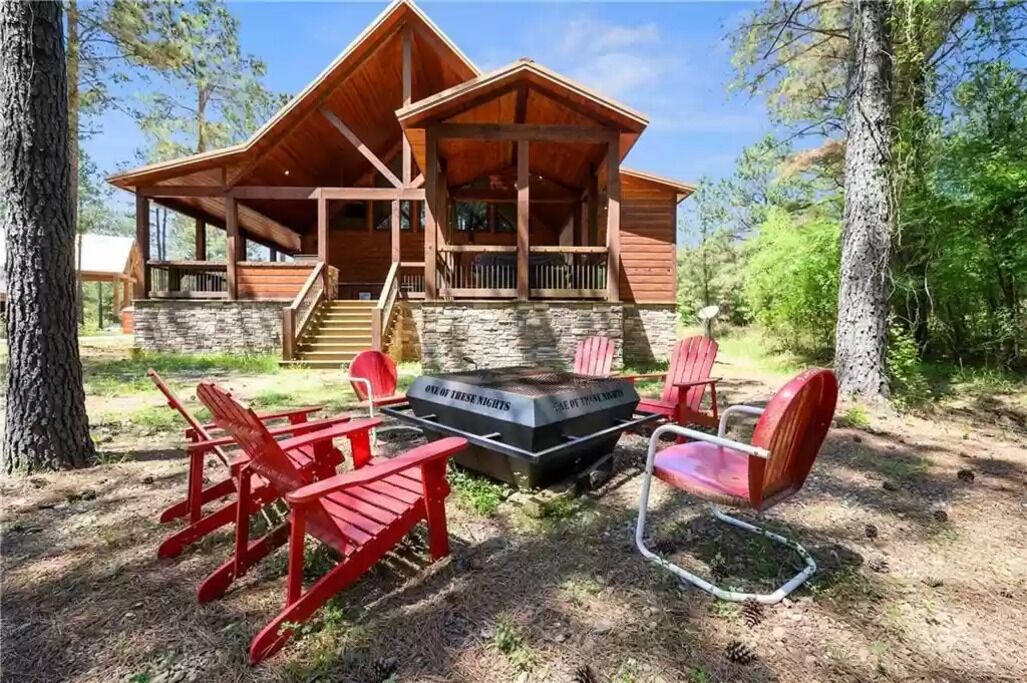 A lodge with a stone foundation, wooden exterior, and a covered porch with red Adirondack chairs.