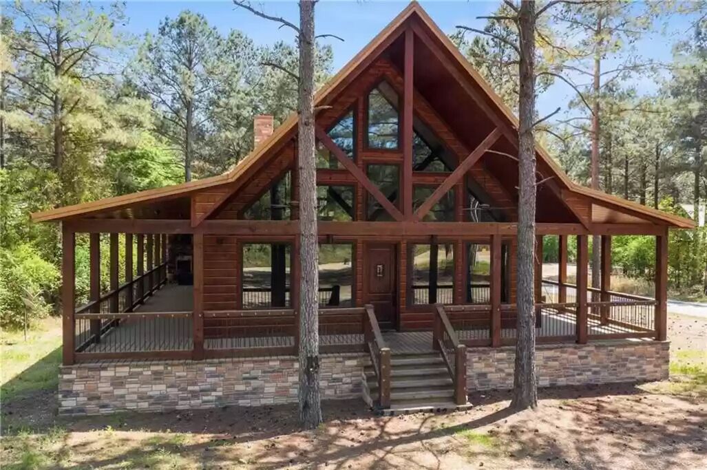 Une cabane en bois avec un toit triangulaire, de grandes fenêtres et des fondations en briques.