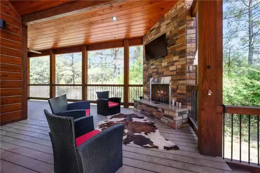Un espacio al aire libre techado con mobiliario de mimbre, una chimenea de piedra y vistas al bosque.