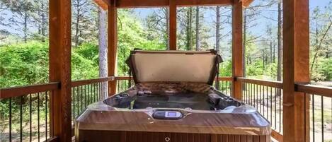 A hot tub in a wooden gazebo with a view of a forest.