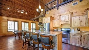 A spacious kitchen with wooden cabinets, a large island with bar stools, and a high ceiling with exposed beams.