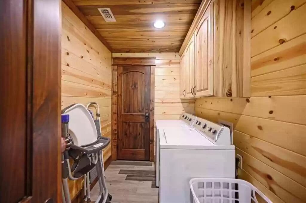 A laundry room with wooden walls and a door, a washing machine, and a drying rack.