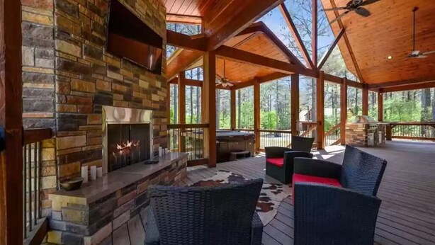 A covered outdoor area with a stone fireplace, wicker furniture, and a view of the forest.