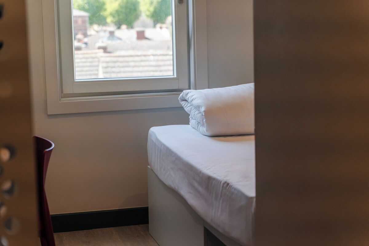 A bedroom with a single bed, a window, and a chair.