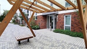 Un patio con una pérgola de madera, un banco y un edificio de ladrillo identificado como “Block C”.