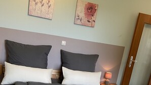 Un lit bien fait, avec une literie grise, deux oreillers et une tête de lit en bois. Deux œuvres d’art sont accrochées au mur au-dessus du lit.